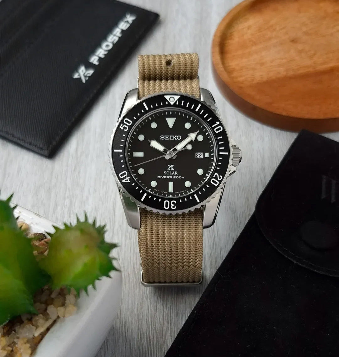 A Seiko Solar dive watch with a black dial and bezel, a silver stainless steel case, and a tan WIS Watch Strap