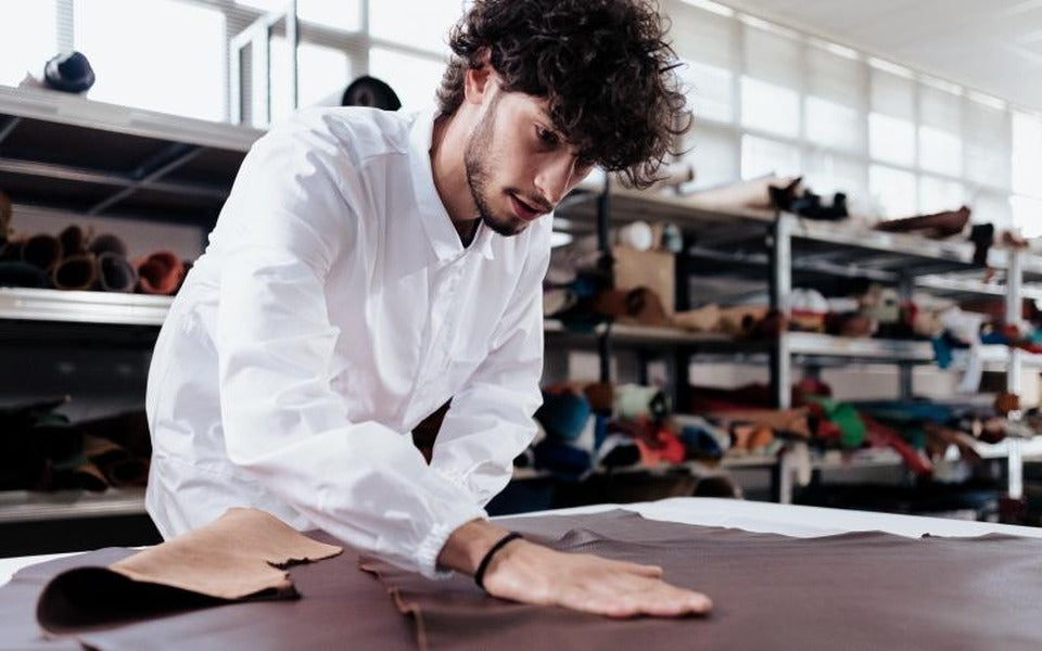 A craftsman inspecting leather hides on a cutting table