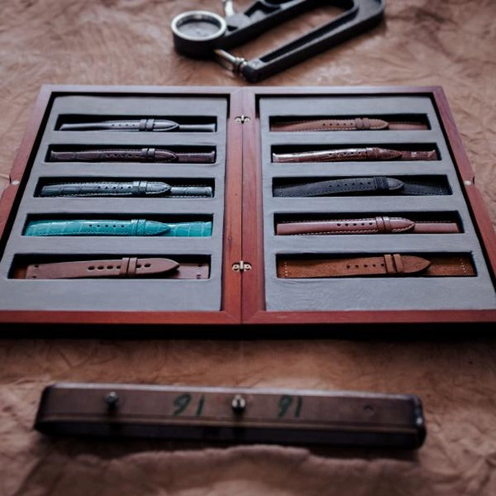 A wooden tray of finished leather watch straps ready for quality control